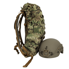 The OPE Gear Backpack Scrim - Camouflage Pack Cover by OPE Gear is shown standing upright beside a matte tan military helmet with mounting hardware, both set against a plain white background.