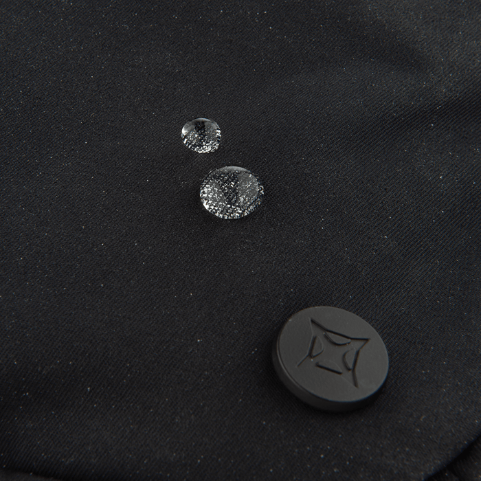 Three water droplets rest on the black fabric of the Vertx Everyday Fanny Pack 2.0, showcasing its water-resistant design by Vertx—making it perfect for off-body concealed carry. A black circular button with a geometric pattern appears at the lower right.