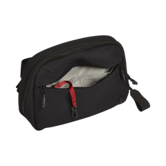 A black Vertx Everyday Fanny Pack+ by Vertx is shown with its main compartment partially open, displaying a gray lining, mesh pocket, and red strap inside. This pouch is ballistic-panel compatible and features a pull tab plus a front zipper.