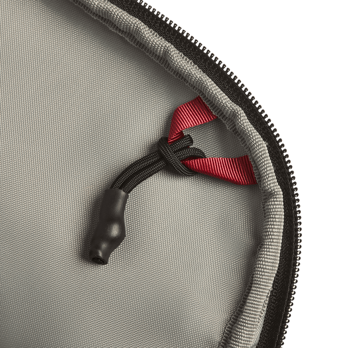Close-up of the Vertx Everyday Fanny Pack+ by Vertx, showing gray fabric, a black zipper, a black cord with a plastic end, and a red ribbon loop—designed to be compatible with ballistic panels for extra protection.