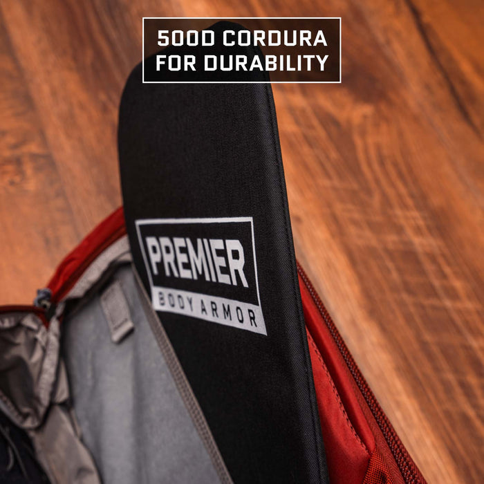 A Multicam Black 9 x 13.5 Level IIIA Armor Insert by Premier Body Armor is shown inside a red backpack on a wooden floor. "500D Cordura for durability" appears above.
